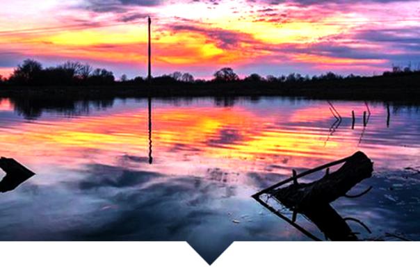 A vibrant sunset over a calm body of water, with the orange, pink, and purple sky reflecting perfectly on the water's surface.