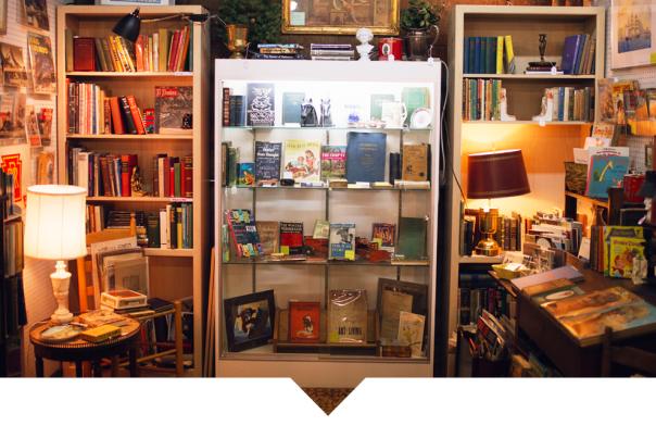 A wooden bookshelf filled with a variety of antique books, framed photographs, and small collectibles.