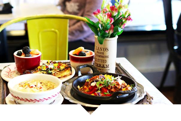 A table setting featuring a vase with flowers next to a small cast-iron skillet of food and a bowl of food.