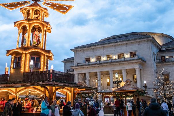 German Christmas pyramid lit in front of large neoclassical building.