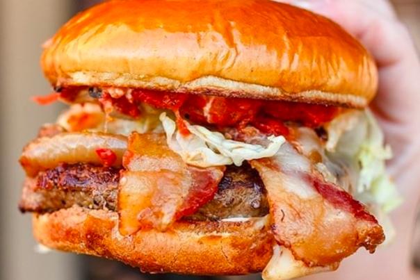 Hand holding a bacon burger in bright colors
