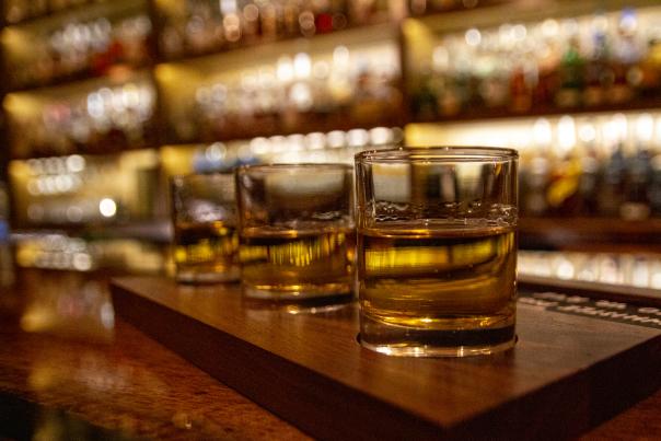 A flight of 3 whiskeys sitting on a bar with blurry lights in the background.