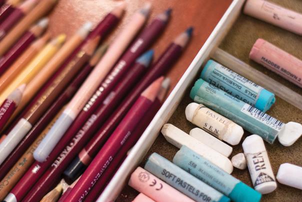 A close-up of colored pencils and chalks arranged in a container, showing multiple shades.