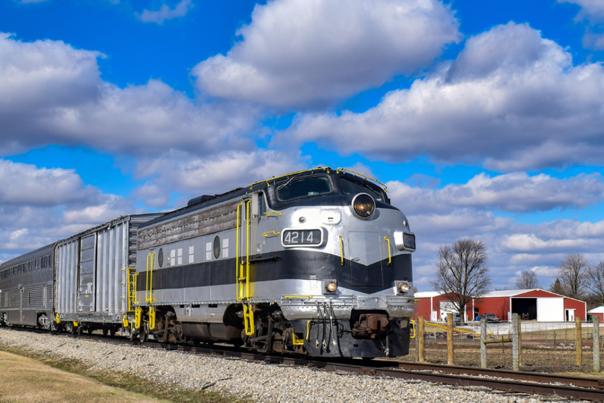 A silver and black locomotive on railroad tracks beneath a partly cloudy sky.