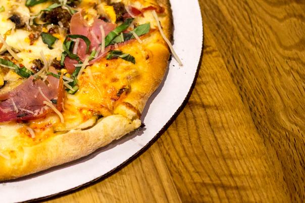 A pizza on circular cardboard, on a wooden serving board.