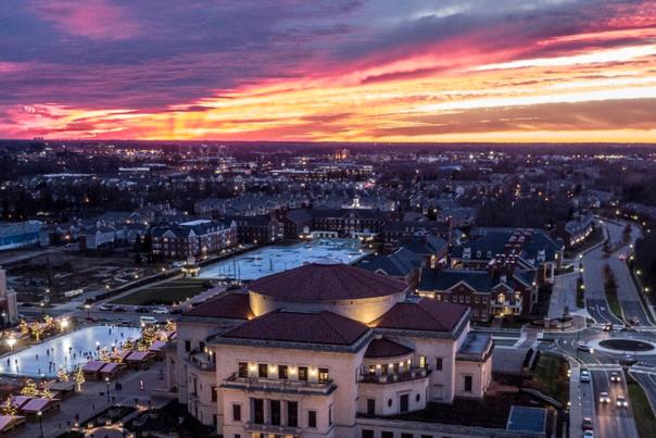 An elevated view of a large building complex at sunset, with warm light and a cityscape in the distance.