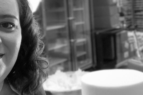 A black-and-white close-up of a person with cakes in the background.