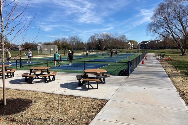 An outdoor scene showing picnic tables and benches next to a pickleball area in Fishers.