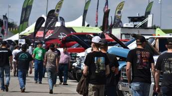 Crowd walks through a vendor area lined with trucks and displays at a diesel motorsports event.