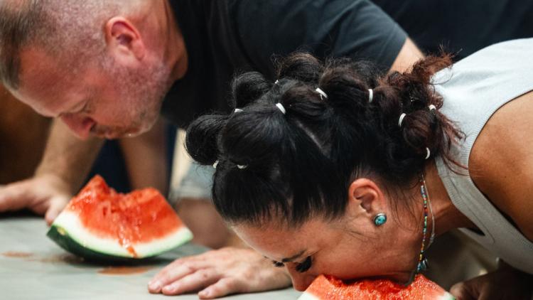 Man and woman leaning over a watermelon during watermelon eating contest