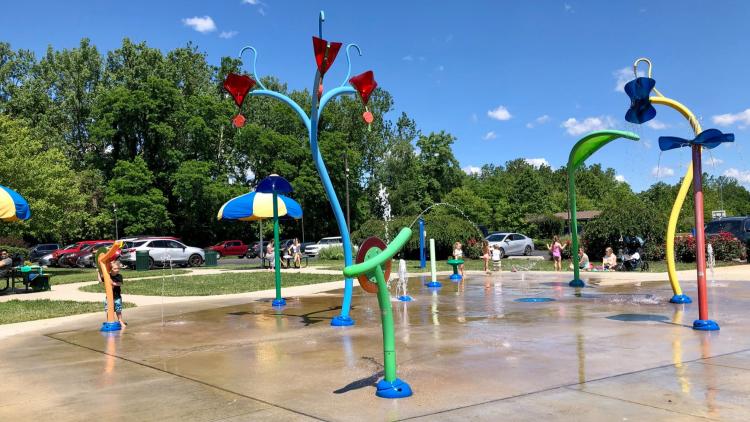 Children play in a colorful outdoor splash pad with fountains and spray features on a sunny summer day in Hendricks County, Indiana.
