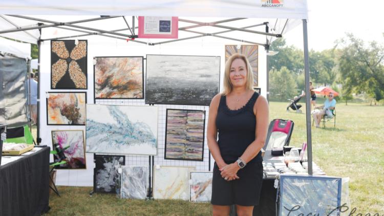 Female artist stands in front of a variety of artwork. (Photo courtesy of the Brownsburg Chamber of Commerce)