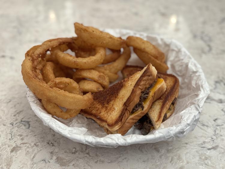 The Braised Beef Grilled Cheese at The Local Kitchen & Tap within the Embassy Suites hotel in Plainfield, served with large onion rings in a basket.