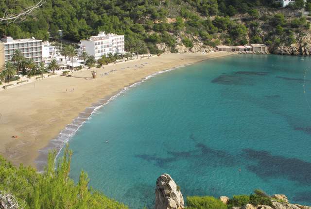 Praia e baía de Cala Sant Vicent com edifícios na frente costeira