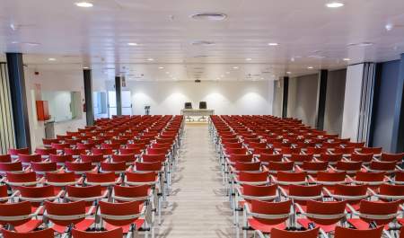 Sala de conferencias preparada para un evento profesional en Ibiza, con filas de sillas rojas orientadas hacia un escenario con mesa de ponentes, en un espacio moderno equipado para congresos, jornadas y ruedas de prensa.
