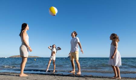 Uma família de quatro pessoas joga à bola numa praia de Ibiza, num dia claro e ensolarado.
