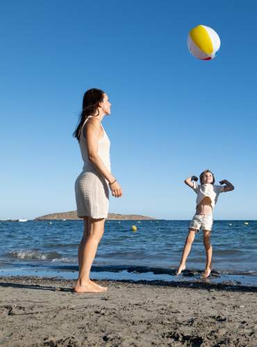Uma família de quatro pessoas joga à bola numa praia de Ibiza, num dia claro e ensolarado.