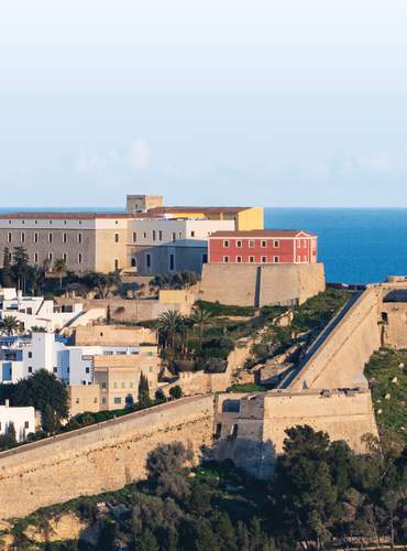 Vista panorâmica de Dalt Vila, a cidade amuralhada de Ibiza, Património Mundial da UNESCO, com as suas muralhas renascentistas, a catedral a dominar a paisagem urbana, casas brancas na sua base e o Mar Mediterrâneo como pano de fundo.