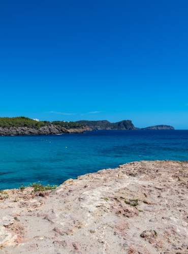 O Mar Mediterrâneo estende-se sob um céu completamente azul numa praia de Ibiza.