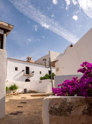 Uma aldeia em Ibiza na primavera, com flores de várias cores, casas de paredes brancas e um céu azul.