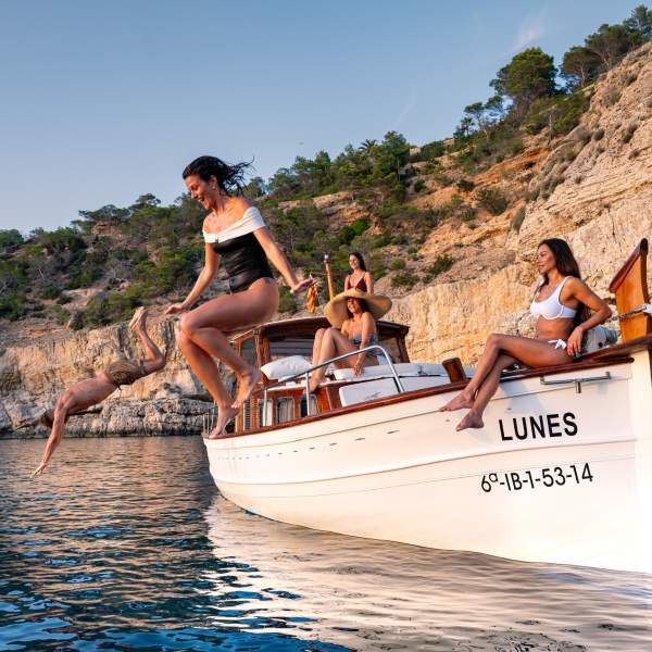 Un grupo de amigos disfruta navegando en aguas de una pequeña cala de Ibiza. Dos de ellos se lanzan al agua desde un llaüt, una embarcación de madera típica de la isla, mientras los otros les observan desde el barco