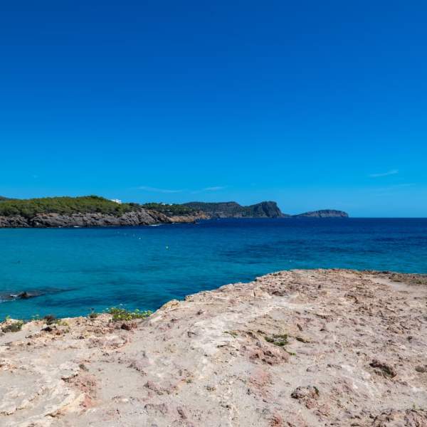 O Mar Mediterrâneo estende-se sob um céu completamente azul numa praia de Ibiza.