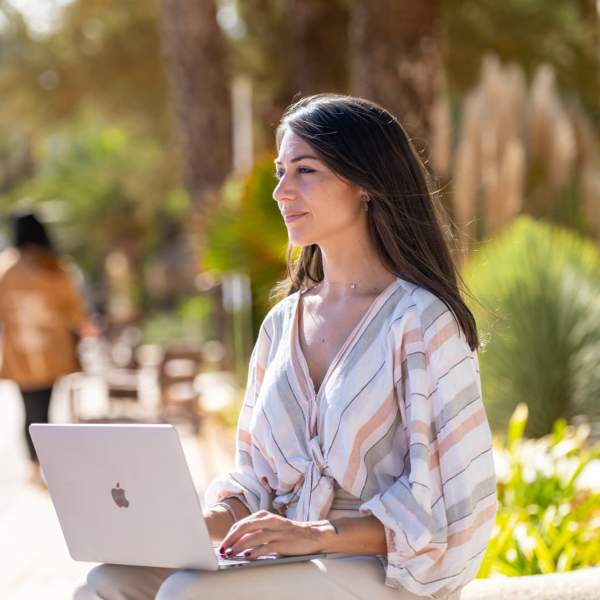 Uma jovem olha para o mar enquanto segura um computador, sentada num passeio à beira-mar em Ibiza.