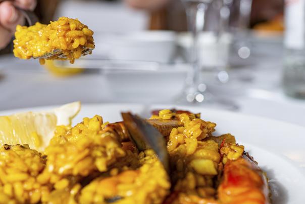Primer plano de un plato de arroz marinero servido con marisco y una rodaja de limón, mientras una persona sostiene una cucharada del arroz en un restaurante de Ibiza, mostrando la gastronomía mediterránea de la isla.