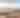 Serene sandy dunes rise beside a calm lake, with gentle waves reflecting a pastel sunset sky. Lush greenery frames the scene.