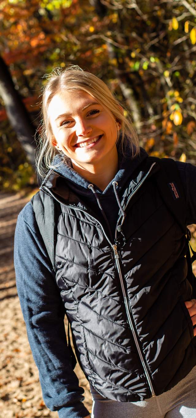 A blonde woman stands on a trail with fall colors
