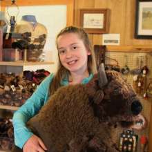 A young girl in a turquoise shirt holds a large bison stuffed animal