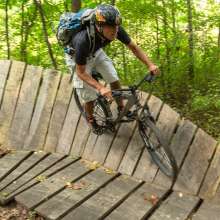 A man wearing a helmet rides a mountain bike on a wooden raised trail