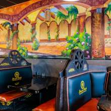 Black stylized booths with wagon wheel decorations line the wall. A mural with a patio building and flowers is on the wall.