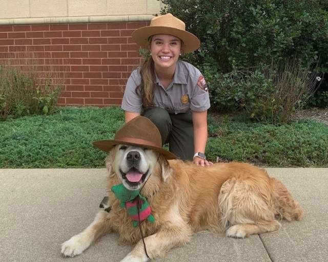 A dog with a park ranger hat sits in front of a park ranger