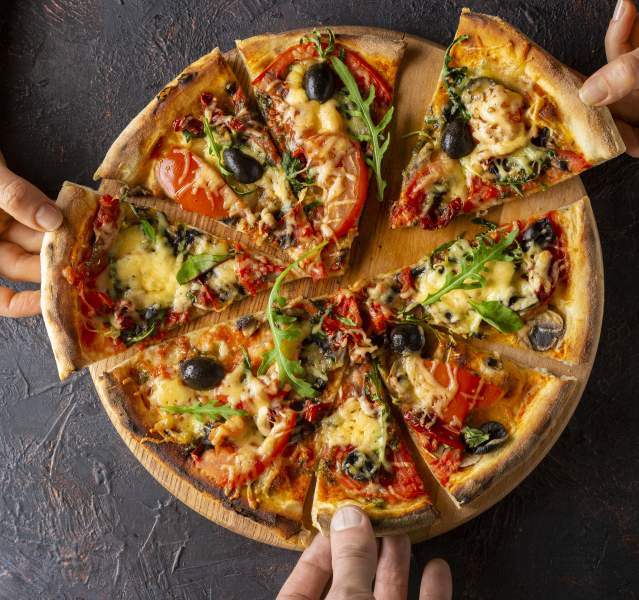 Three hands are reaching to each grab a piece of pizza.