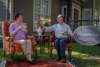 A man and women sit on furniture drinking tea while sitting on the front lawn.