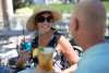 A woman in a hat and sunglasses holds a glass while smiling
