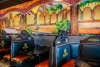 Black stylized booths with wagon wheel decorations line the wall. A mural with a patio building and flowers is on the wall.
