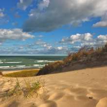 Sandy dunes with beach grass in the foreground and Lake Michigan visible under a partly cloudy sky at Indiana Dunes