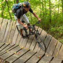 A man wearing a helmet rides a mountain bike on a wooden raised trail