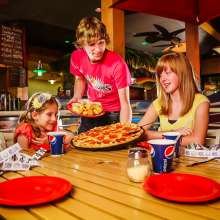A waiter in a red shirt serves pizza to two young girls
