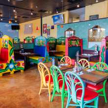 Colorful chairs, booths, and table are inside a restaurant. A mural and television are in the background.