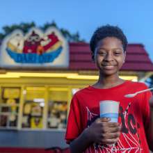 A young boy eats a shake in front of an ice cream stand.