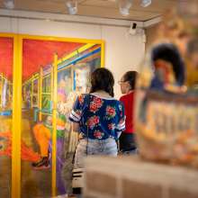 Two people look at a brightly colored painting on the wall. A blurred statue is in the foreground.