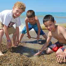 Three young boys play in the sand near the shoreline