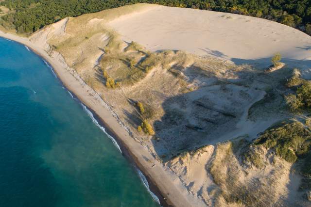 Aerial view of a parabolic dune along bright blue Lake Michigan.
