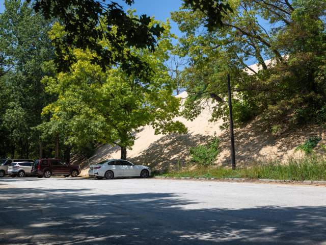 Cars are parked in a lot in front of a giant dune.