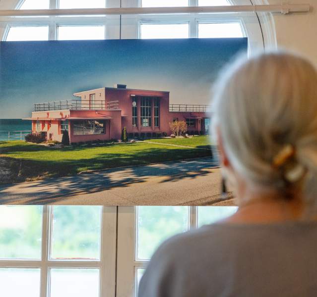 The back of a woman's head is seen as she looks at a painting of the Florida House in the Indiana Dunes.