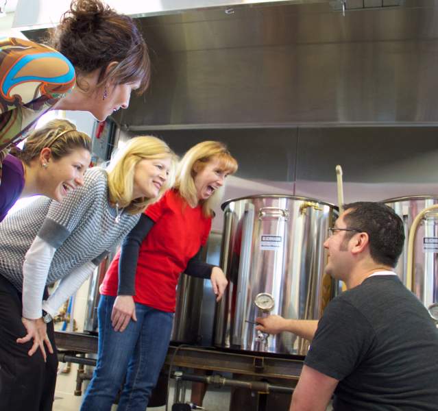 A group stand around a man kneeling down while showing them brewery tools