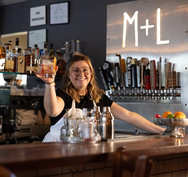 A bartender hold up a glass while standing behind the bar